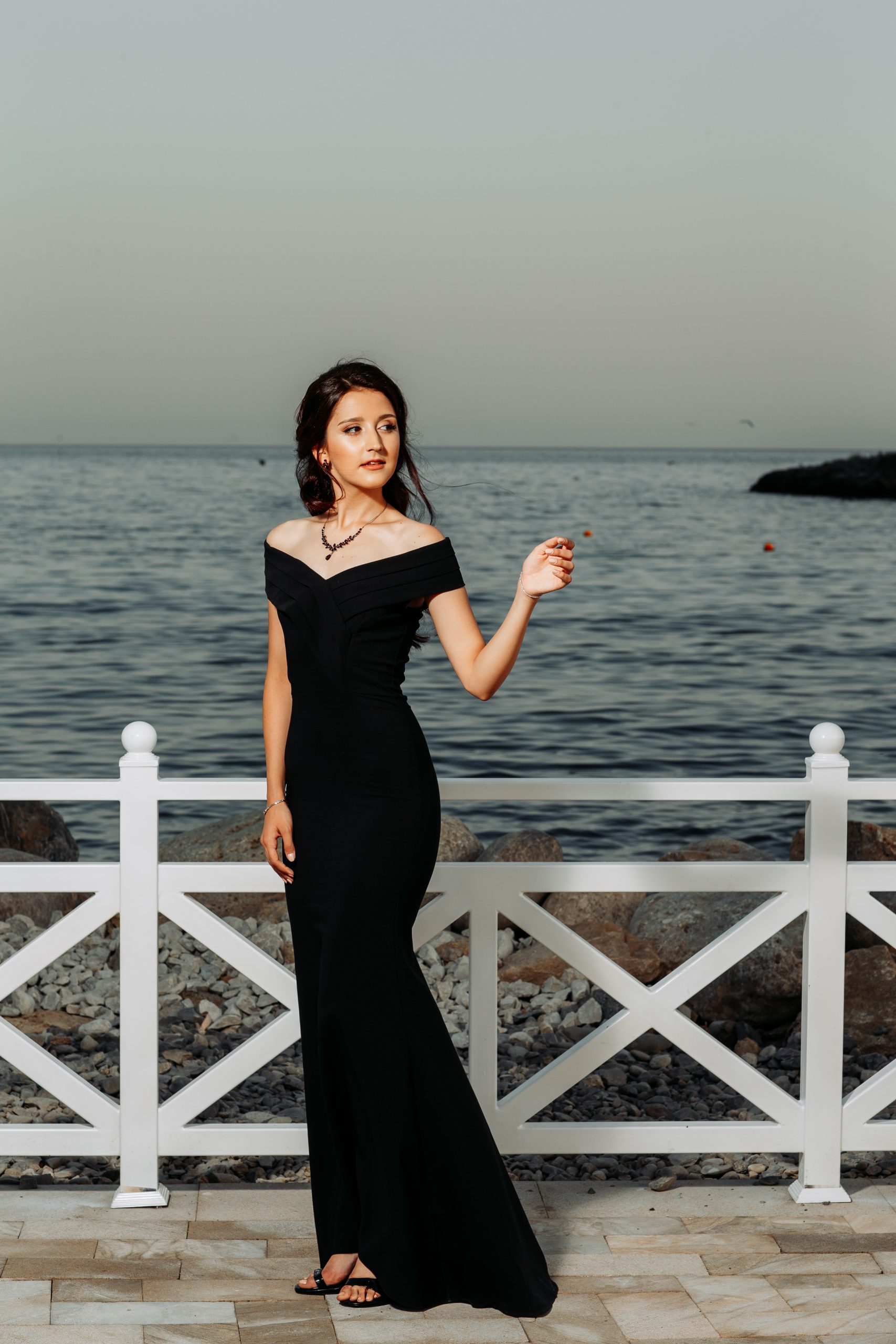 beautiful girl standing in long black dress in near the seaside during daytime .